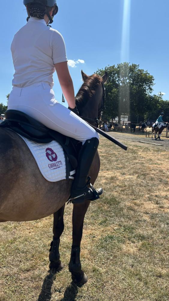 Rider in competition dress on a horse wearing a white Cavaletti Collection saddle pad