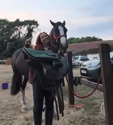 Rider standing beside a horse while adjusting tack outdoors near a fence line Cavaletti Collection.