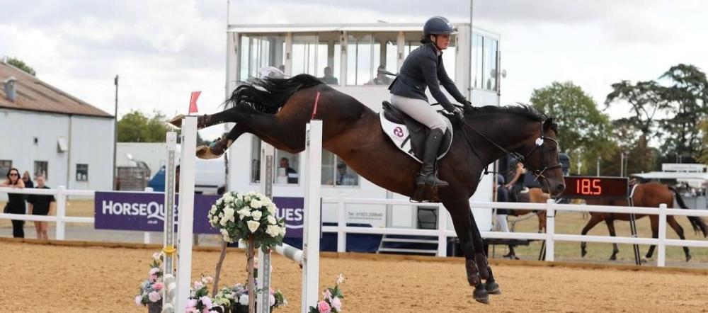 Rider and horse clearing a floral show jump fence in competition