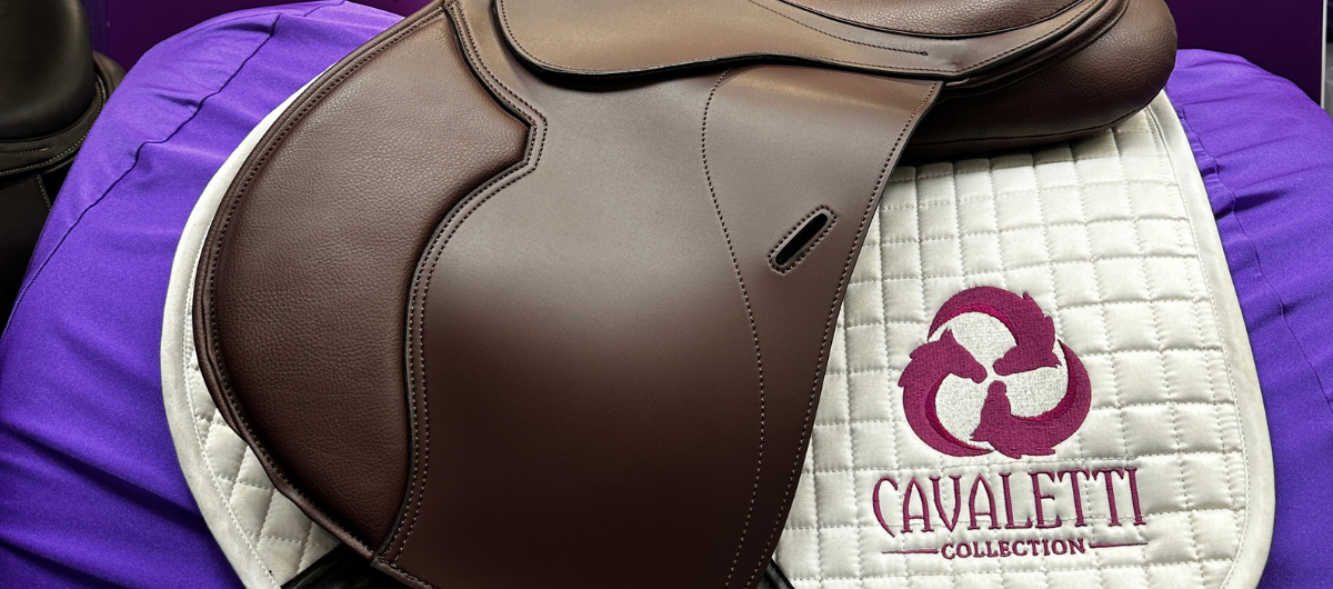 Close‑up of a brown Cavaletti Collection saddle on a white quilted pad with branded embroidery.